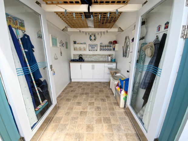 Inside Hut Eleven — a small kitchenette with a gas ring and kettle, coat hooks either side, and beach kit stored under the bench.