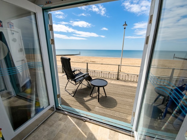 View from the open doors of Hut Eleven straight out to the sea and beach at Southbourne, with a deckchair and side table on the deck.